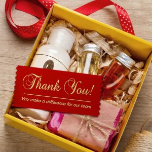 An open gift box filled with items that has a badge ribbon resting on top with a thank you message.