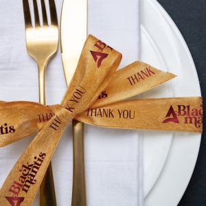 A dinner place setting featuring a ribbon bow, imprinted with a thank you message.